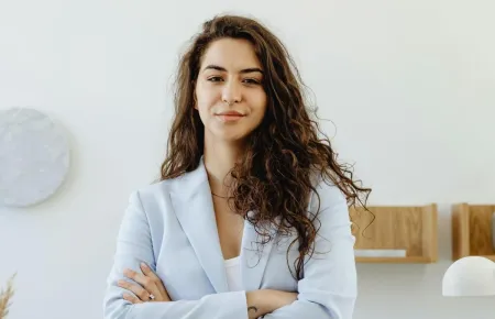 A woman wearing a pale blue blazer standing confidently with her arms folded | What does a CEO do?